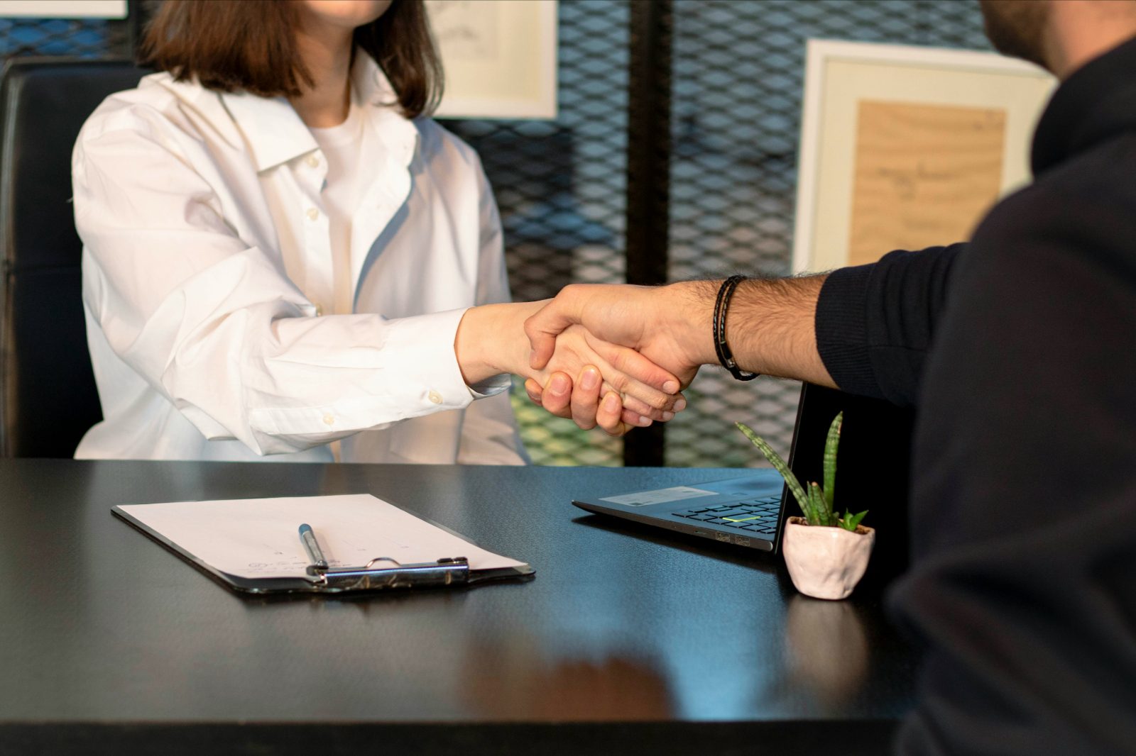 Two people shaking hands over a desk after agreeing to work together