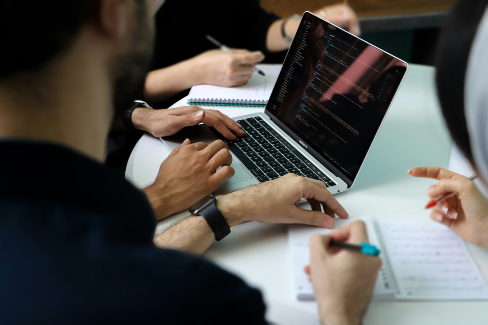 A team reviewing code together on a laptop while taking notes