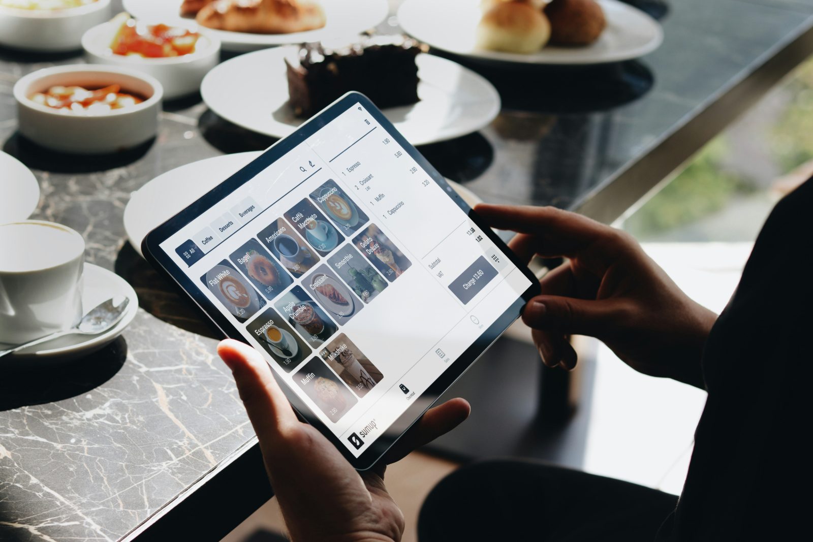 Person using a point-of-sale ordering app on a tablet in a cafe